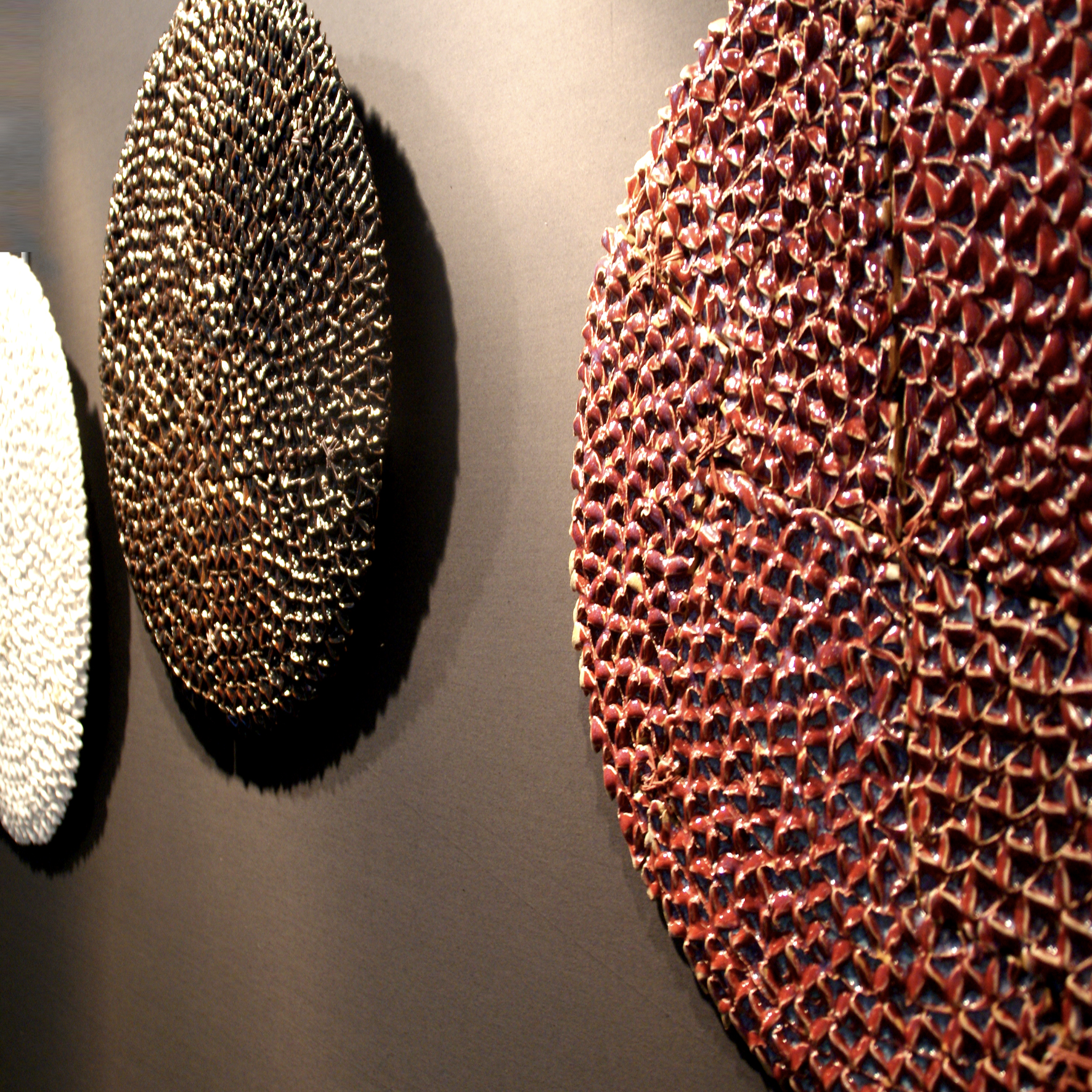 gRAteR — rij ronde schijven met noppenreliëf in terracotta, brons en wit tegen een donkere wand
